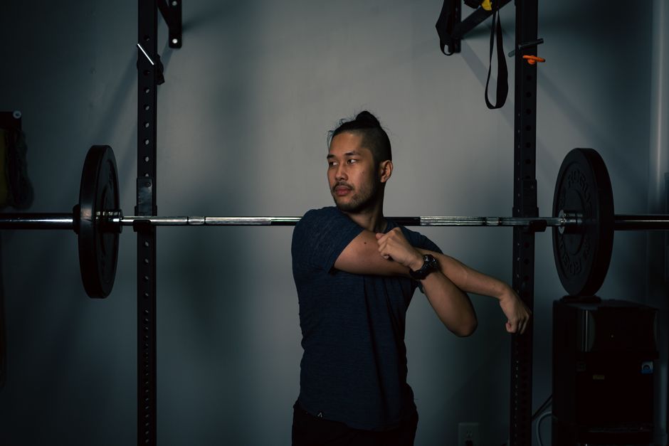 Homem ajustando o ombro durante um treino de musculação em um ambiente de academia com equipamento de peso ao fundo.