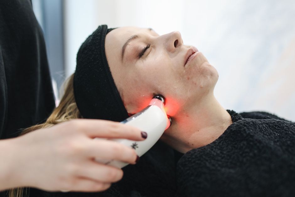 Imagem de uma mulher recebendo tratamento facial com luz vermelha em um procedimento estético de cuidados com a pele.