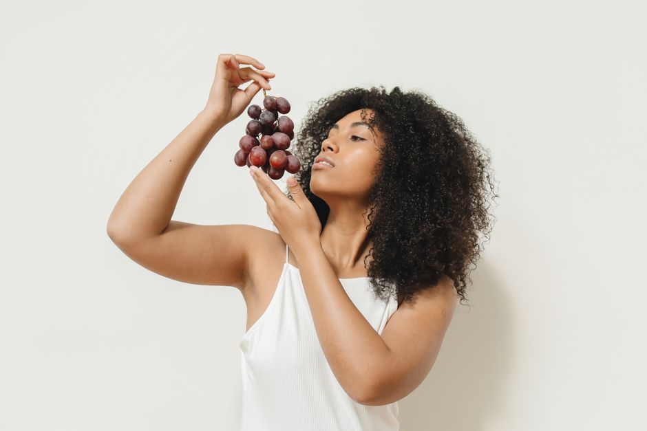 Mulher segurando um cacho de uvas, simbolizando saúde e alimentação natural, em um estilo minimalista e elegante para blog de bem-estar.