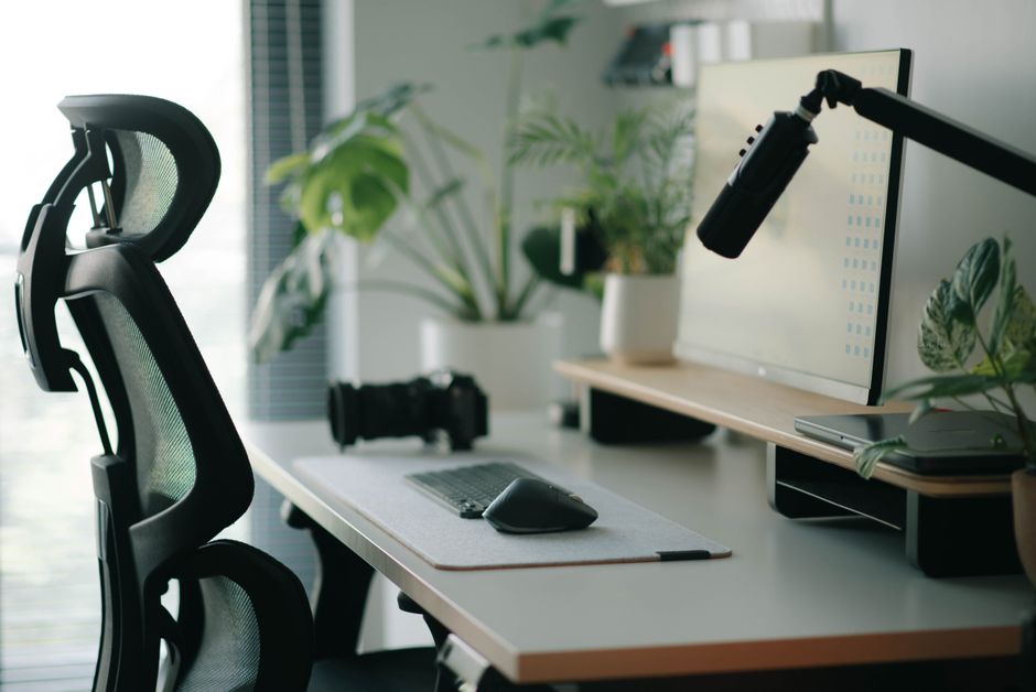Imagem de um ambiente de trabalho moderno com mesa de escritório, monitor, cadeira ergonômica e plantas, ideal para artigos sobre home office e produtividade.