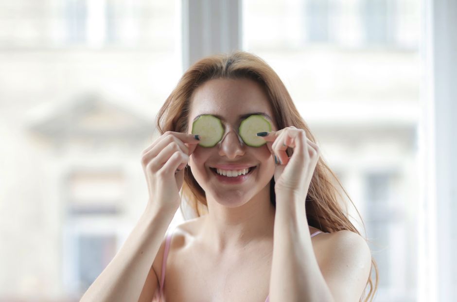 Mulher sorridente segurando rodelas de pepino sobre os olhos, em clima de cuidado com bem-estar e beleza.