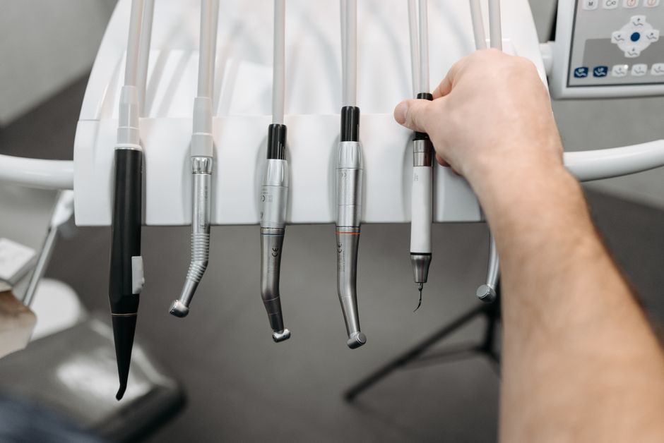 Imagem de instrumentos odontológicos utilizados em procedimentos médicos ou dentários, organizados em uma bandeja ao lado de um monitor de diagnóstico.