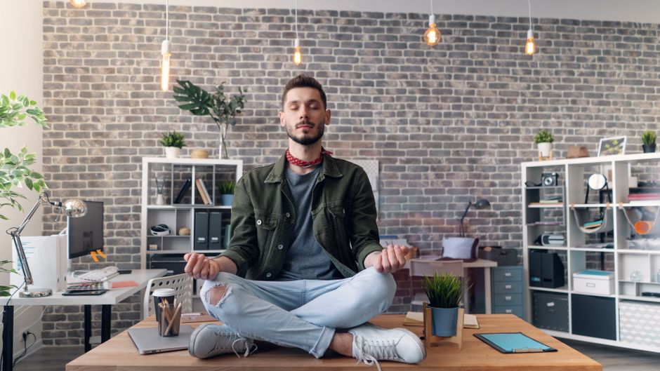 Jovem meditando no escritório, promovendo bem-estar e equilíbrio entre produtividade e saúde mental no ambiente de trabalho.