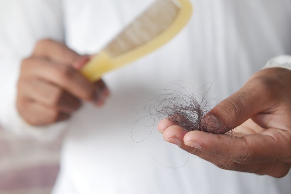 Pessoa removendo fio de cabelo de um pente, ilustrando cuidados pessoais e higiene capilar.