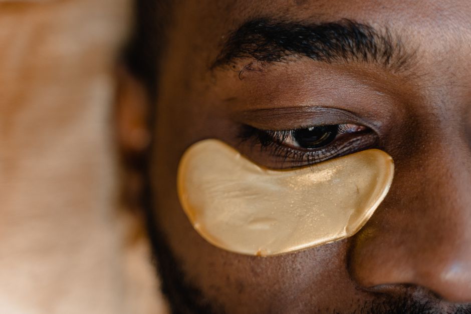 Close-up de uma pessoa com compressa de ouro sob o olho, simbolizando cuidados com a saúde da pele e tratamentos estéticos faciais.