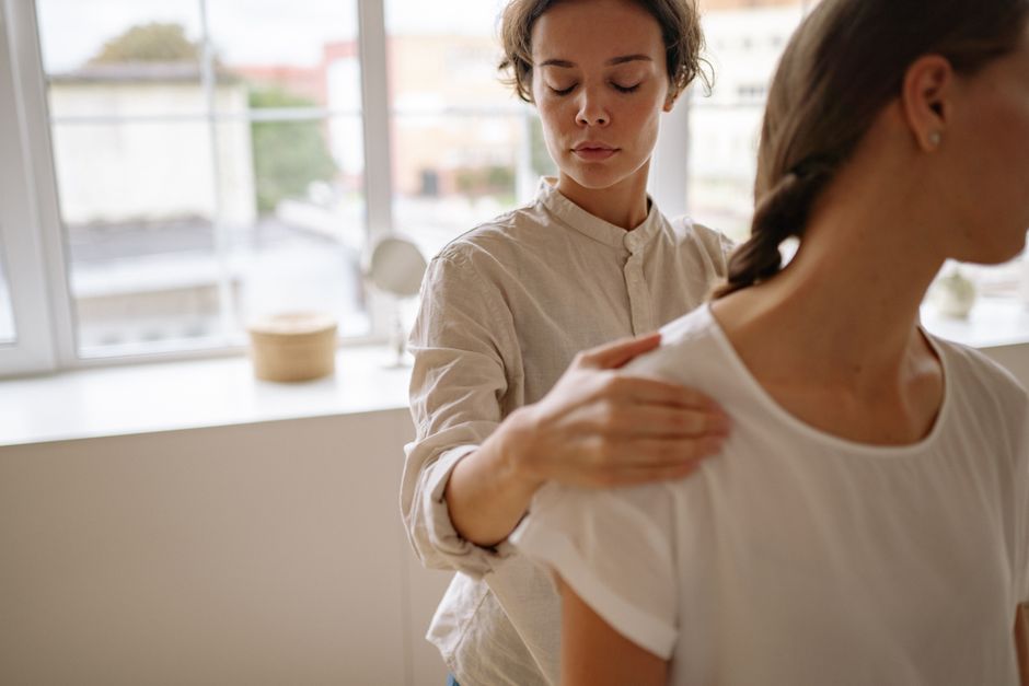 Mulher realizando uma massagem relaxante em outra pessoa em um ambiente iluminado naturalmente, foco no momento de bem-estar e cuidado pessoal.