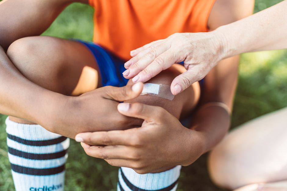 Pessoa sendo atendida por um profissional de saúde ao receber uma bandagem na perna ao ar livre, destacando cuidados médicos e bem-estar infantil.