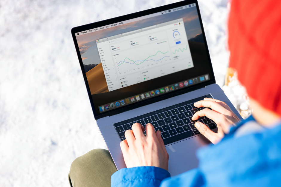 Pessoa analisando gráficos de desempenho financeiro em um laptop ao ar livre, simbolizando monitoramento de dados e estratégia de negócios.