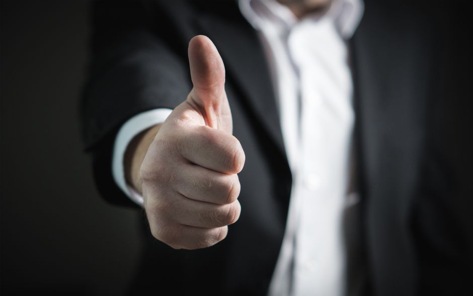 Pessoa de terno dando um joinha, simbolizando aprovação ou sucesso em um contexto profissional ou empresarial.