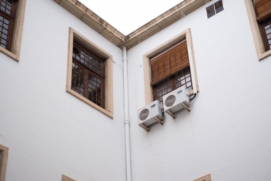 Vista de janelas com persianas e aparelhos de ar-condicionado em um prédio antigo, destacando a ventilação e conforto térmico na arquitetura urbana.