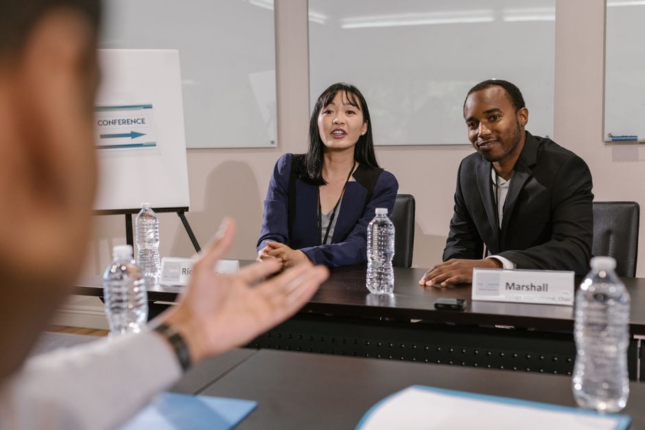 Duas pessoas participando de uma reunião de negócios ou entrevista em um ambiente corporativo, com foco em comunicação e networking.