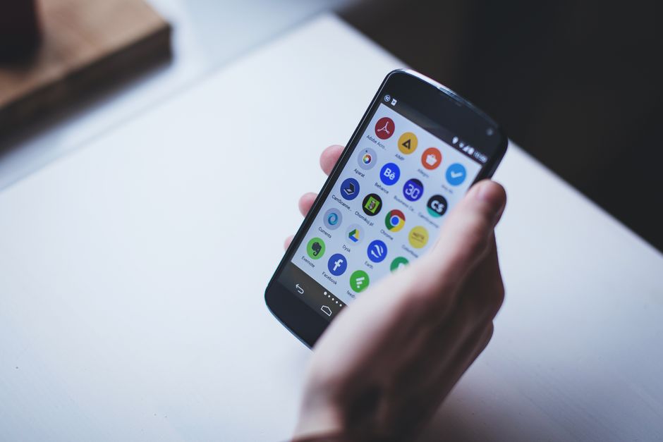 Pessoa segurando um smartphone com diversos aplicativos abertos, representando o uso de tecnologia móvel na rotina diária ou profissional.