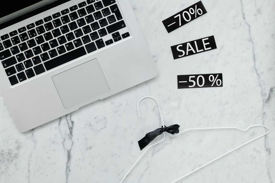 Imagem representando descontos e promoções em uma estratégia de vendas online, com um laptop e etiquetas de desconto em fundo de mármore branco.