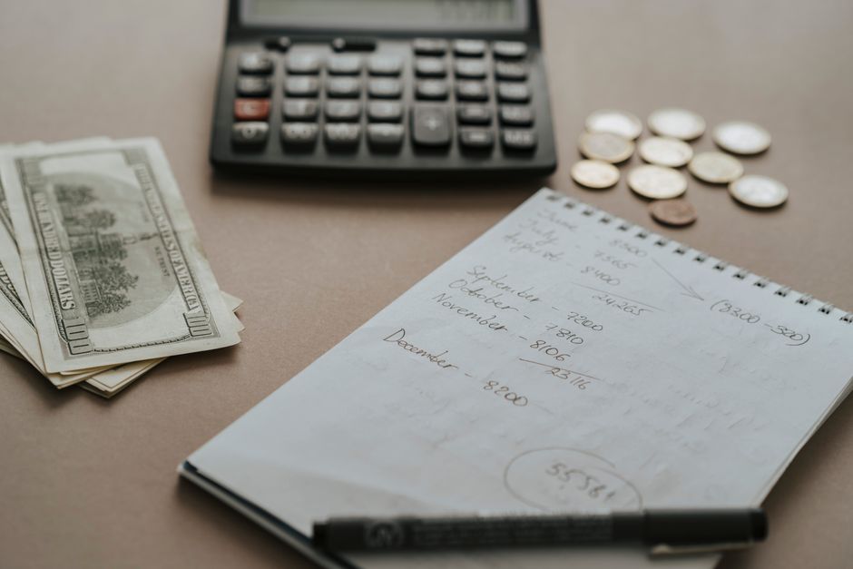Imagem de ambiente de trabalho com calculadora, dinheiro em dólares, anotações financeiras e moedas, ideal para artigos sobre gestão financeira pessoal ou controle de orçamento.