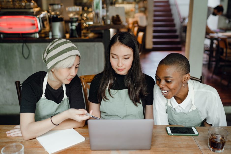 Três pessoas em uma cafeteria participando de uma reunião de trabalho ou estudo com foco na colaboração e tecnologia.