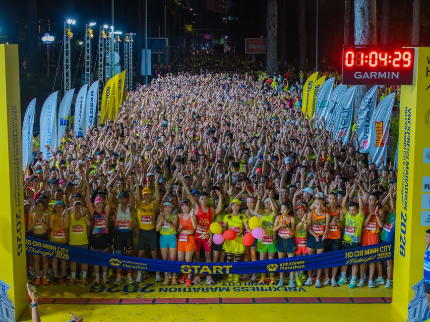 Imagem de uma largada de corrida noturna com dezenas de participantes ansiosos, sob iluminação artificial e painel de tempo digital, simbolizando um evento esportivo na cidade de Ho Chi Minh em 2026.