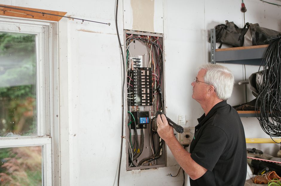 Homem realizando manutenção elétrica em quadro de disjuntores em ambiente de oficina ou instalação residencial.