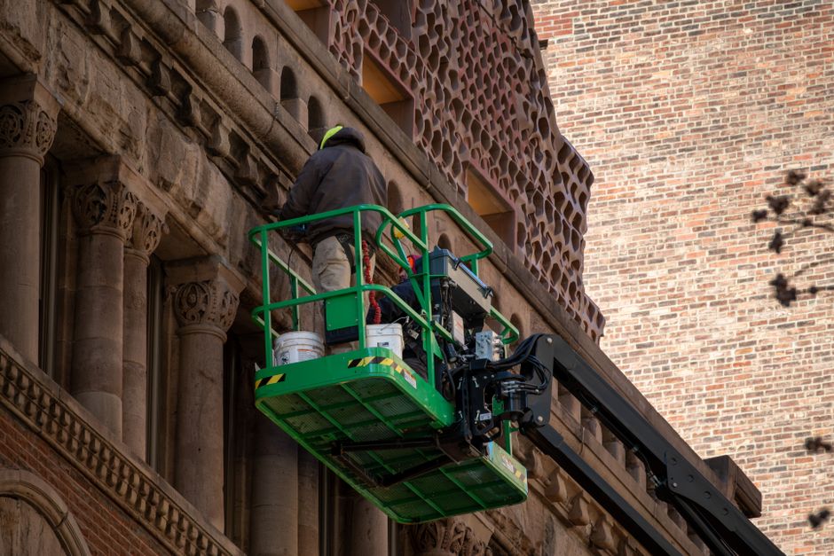 Técnico realizando manutenção em fachada de edifício antigo utilizando equipamento de elevação suspenso.
