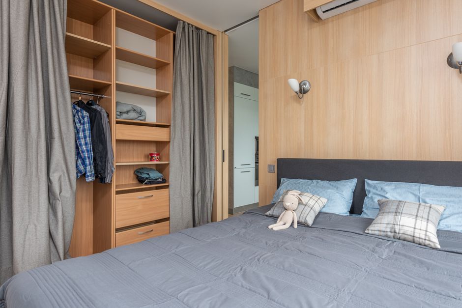 Quarto moderno com detalhes em madeira, cama de casal arrumada com travesseiros e um personagem de pelúcia, transmitindo conforto e aconchego para um artigo sobre decoração e organização de ambientes.