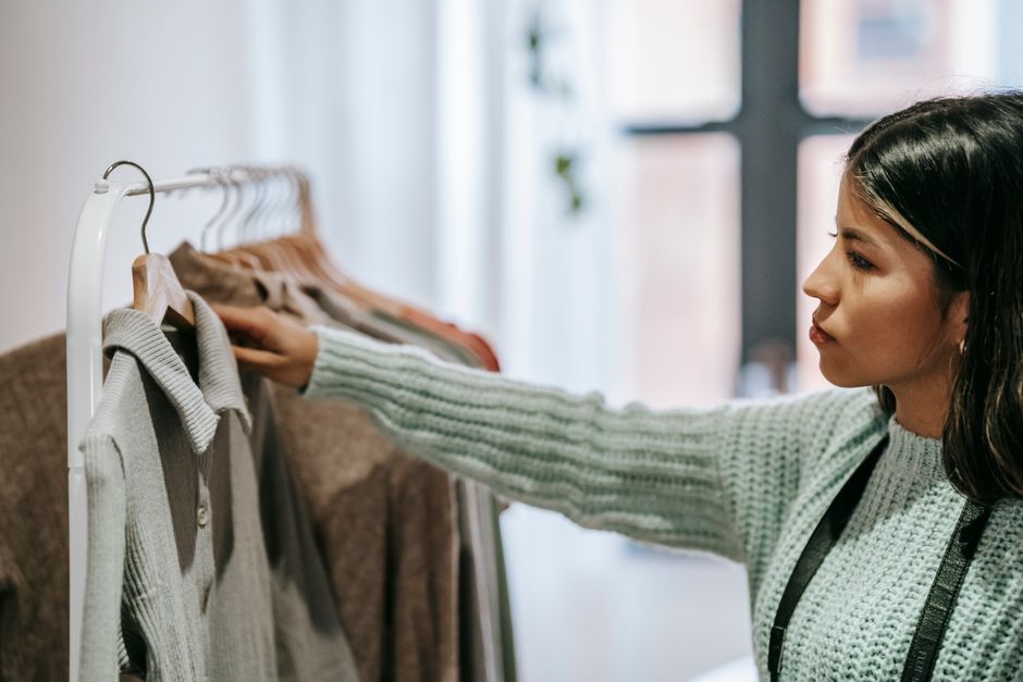 Mulher escolhendo roupas em uma loja de roupas, refletindo sobre moda e compras.