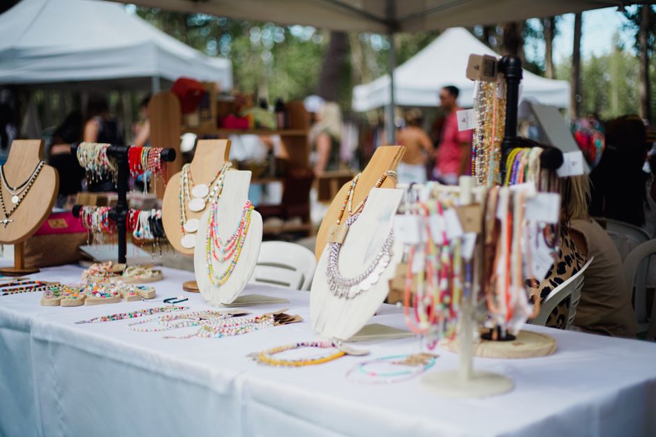Feira ao ar livre exibindo acessórios de moda e bijuterias artesanais, com visitantes explorando os produtos sob tendas.