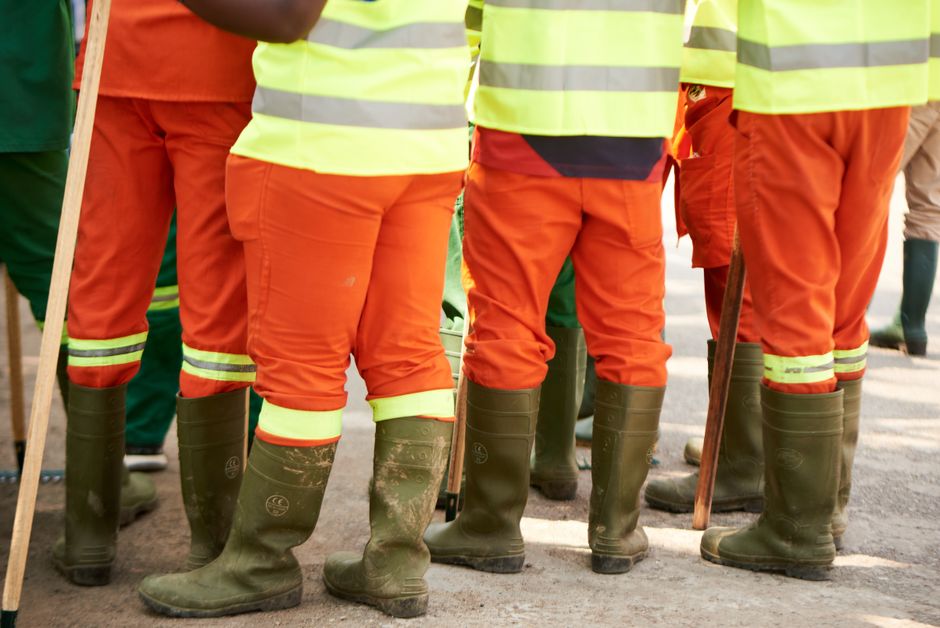 Grupo de trabalhadores usando roupas de segurança e botas de borracha, possivelmente em uma atividade de construção ou manutenção ao ar livre.