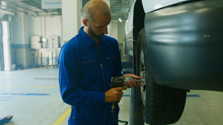 Imagem de um técnico mecânico realizando manutenção em um carro em uma oficina automotiva, focada no procedimento de reparo e inspeção de veículos.