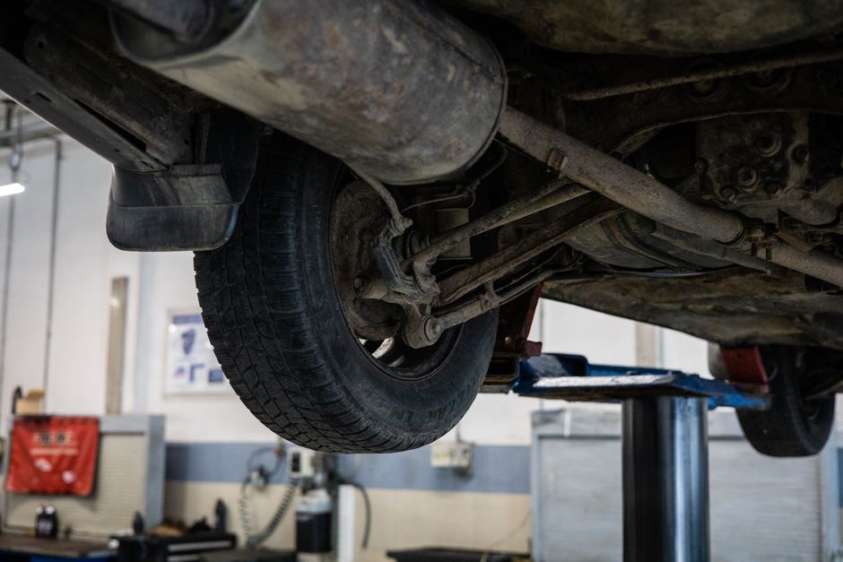 Imagem de um veículo elevado em uma oficina mecânica, destacando a parte inferior do carro e o sistema de suspensão e rodas.