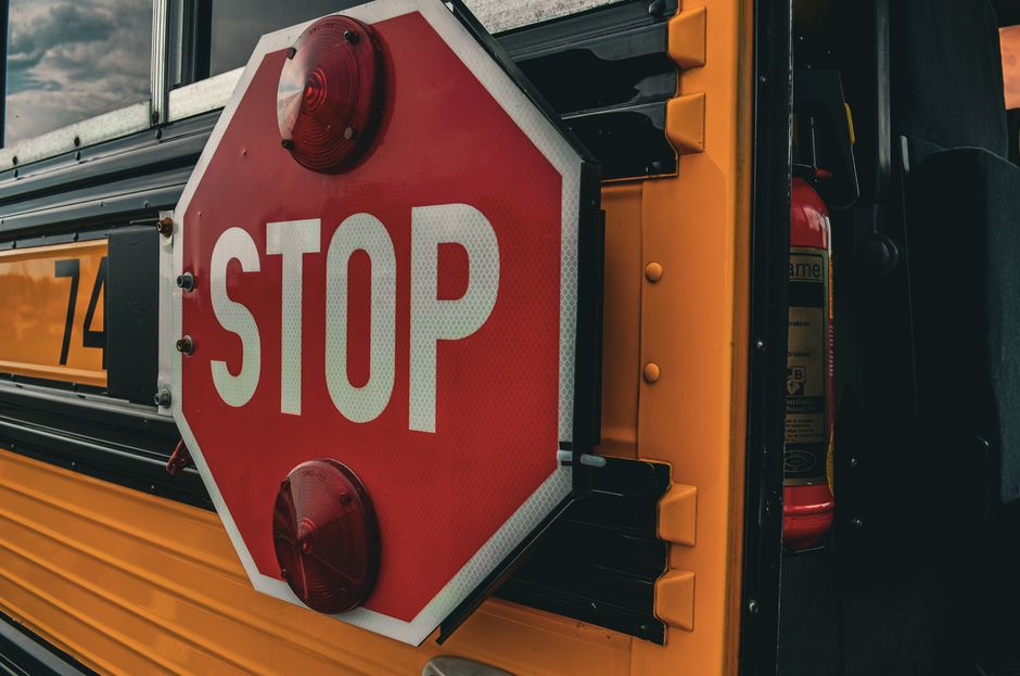 Imagem de uma placa de pare em um ponto de ônibus escolar, alertando para a segurança e prevenção de acidentes.