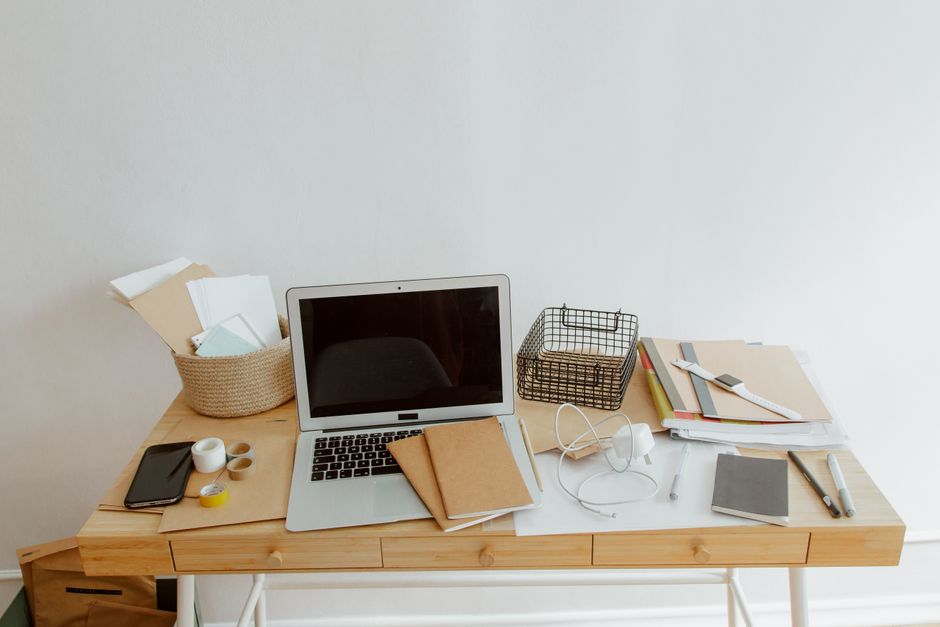 Imagem de uma mesa de trabalho organizada com laptop, documentos, materiais de escritório e objetos pessoais, ideal para ilustrar produtividade e ambiente de trabalho remoto ou estudo.