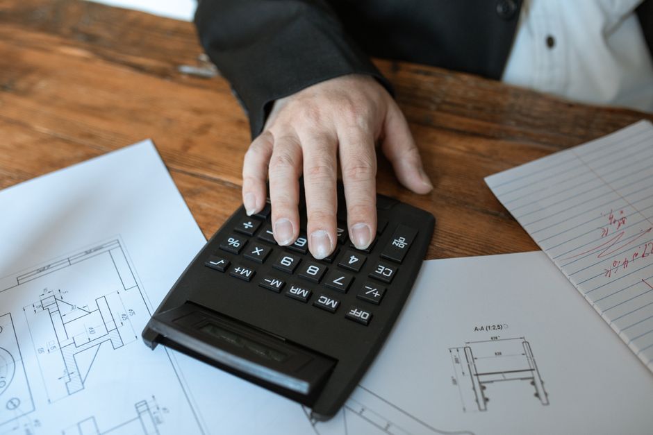 Imagem de uma pessoa utilizando uma calculadora para fazer cálculos relacionados a engenharia ou arquitetura, destacando análise de projetos e planejamento financeiro técnico.