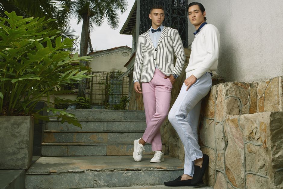 Dois jovens homens estilosos posando ao ar livre, destacando moda casual sofisticada em um ambiente ao ar livre com vegetação e arquitetura moderna.