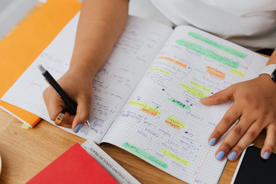 Pessoa organizando e revisando anotações coloridas em um caderno de estudos ou planejamento, focando na gestão de tarefas ou projetos pessoais e profissionais.