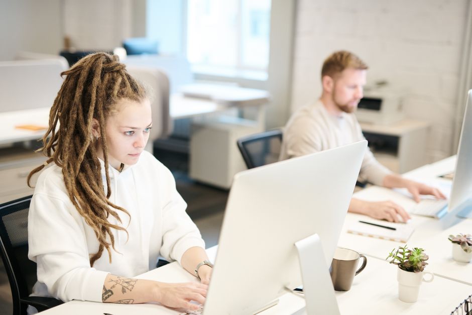 Jovens profissionais concentrados trabalhando em computadores em um ambiente de escritório moderno, refletindo produtividade e colaboração.