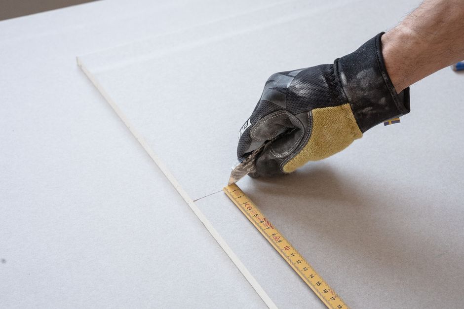 Imagem de um trabalhador medindo uma superfície com régua, indicando precisão e planejamento em uma atividade manual ou de construção.