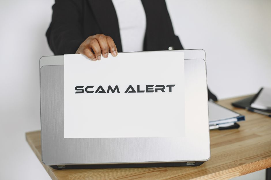 Pessoa segurando um laptop com uma mensagem de alerta de golpe ou scam, indicando preocupação com fraudes online.