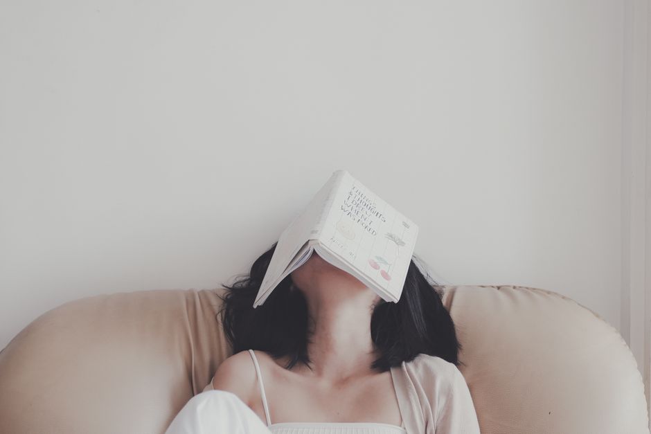 Mulher descansando com um livro na cabeça, transmitindo a ideia de relaxamento ou pausa na rotina de leitura ou estudo.