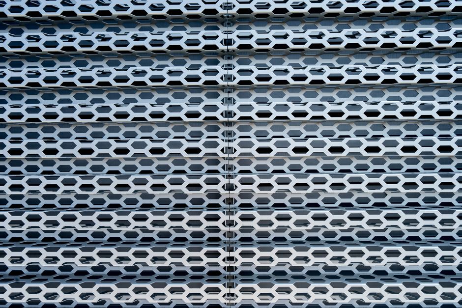 Fachada de edifício com painel metálico decorativo com padrão hexagonal, destacando elementos arquitetônicos modernos.