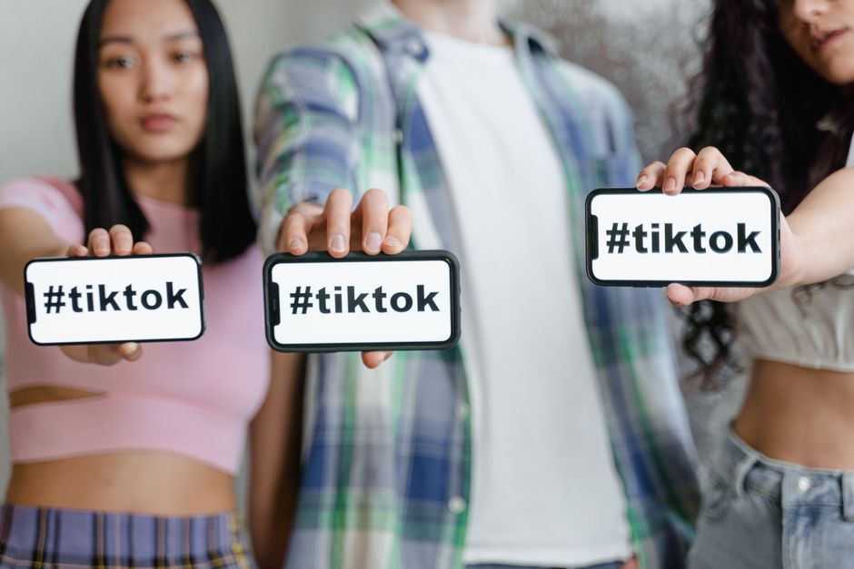 Grupo de jovens mostrando smartphones com a hashtag #tiktok, destacando o impacto das redes sociais na cultura contemporânea.