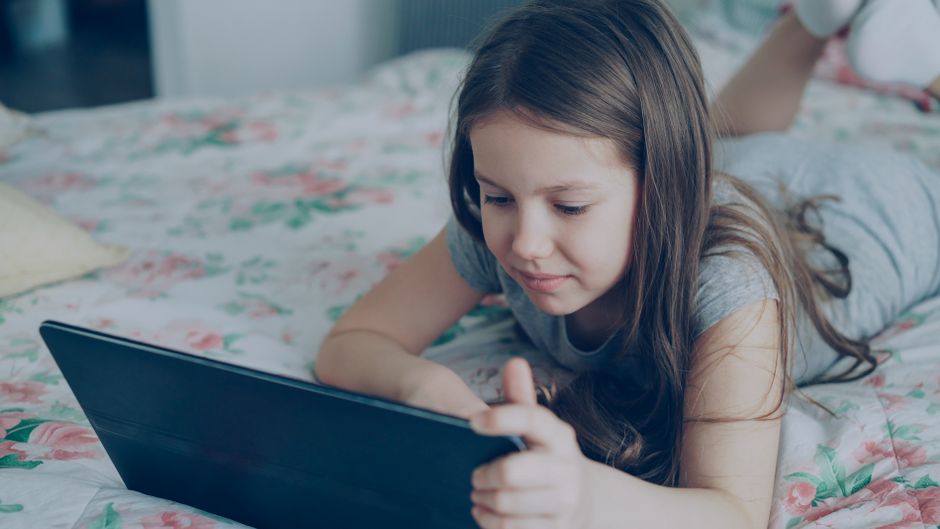 Menina jovem assistindo a conteúdo digital relaxando na cama em um ambiente doméstico.