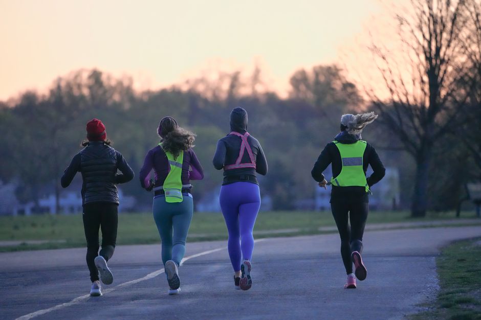 Mulheres praticando corrida ao ar livre ao entardecer, em um parque com árvores e céu ao fundo.