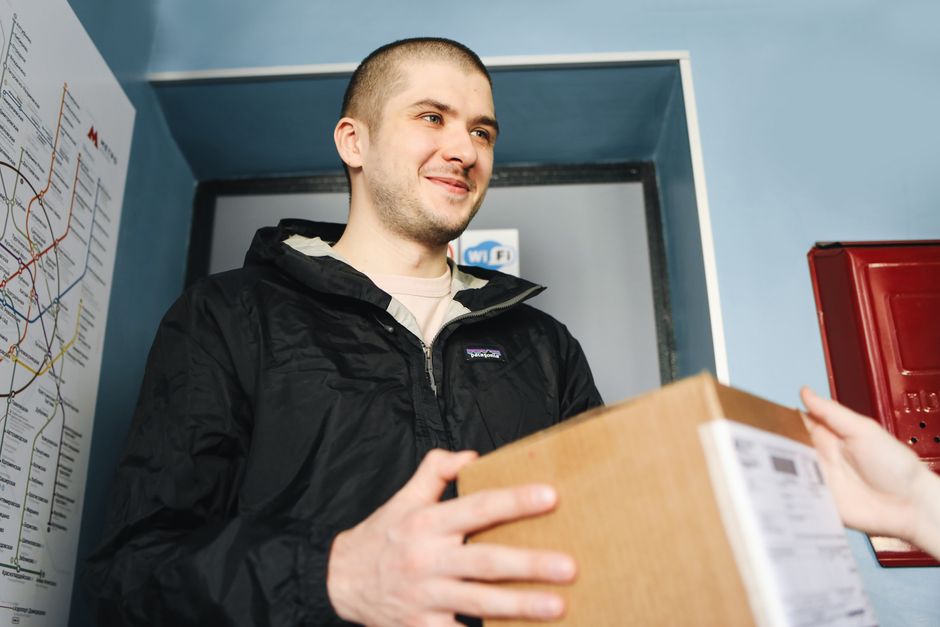 Homem entregando um pacote em ambiente de correio ou entrega, representando serviço de logística ou envio de encomendas.
