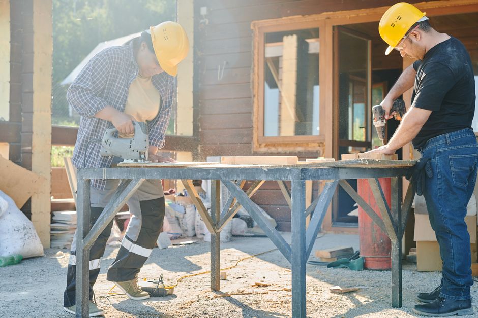 Dois trabalhadores construindo uma estrutura de madeira ao ar livre, usando ferramentas elétricas em um projeto de construção residencial.