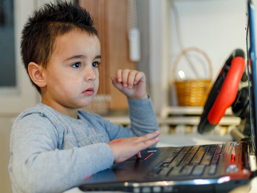 Criança assistindo ou jogando com um computador portátil em um ambiente doméstico.
