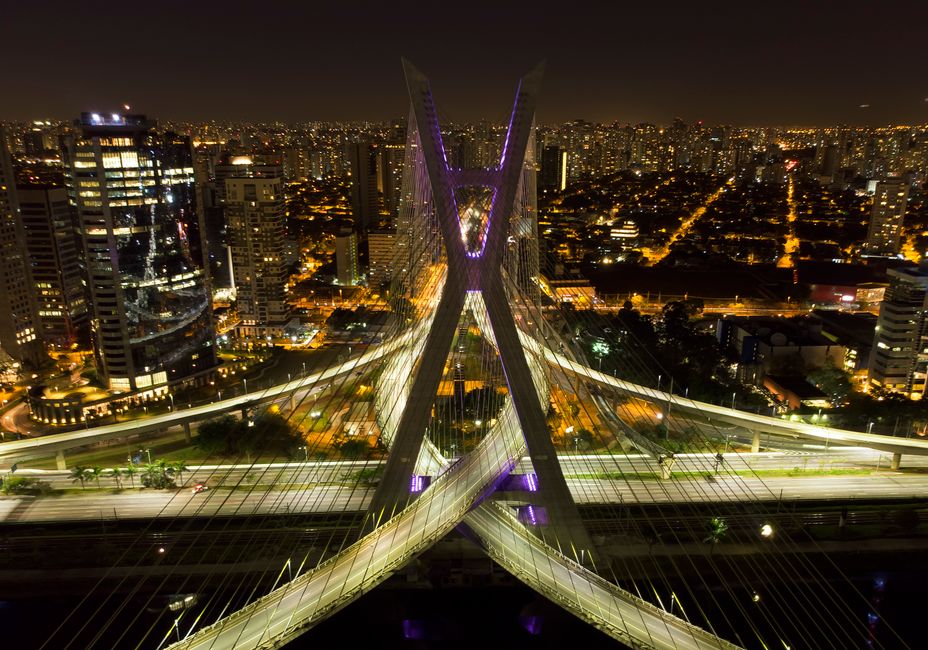 Vista aérea noturna de uma cidade moderna destacando uma ponte icônica com iluminação, representando inovação urbana e arquitetura contemporânea.