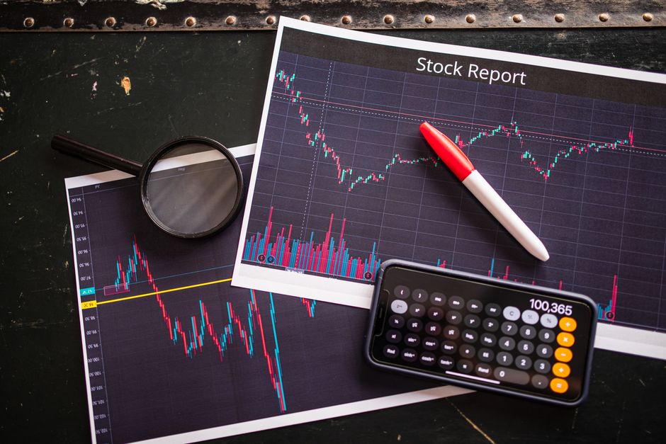 Imagem de relatório de ações com gráficos de mercado, calculadora e lupa, ilustrando análise financeira e investimentos.