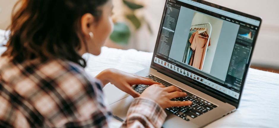 Mulher trabalhando com edição de fotos de moda em um laptop, focada em gestão de conteúdo visual para blogs de moda ou marketing digital.