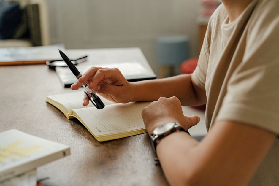 Pessoa organizando suas tarefas e planejamentos com caderno e caneta, em um ambiente de trabalho ou estudo.