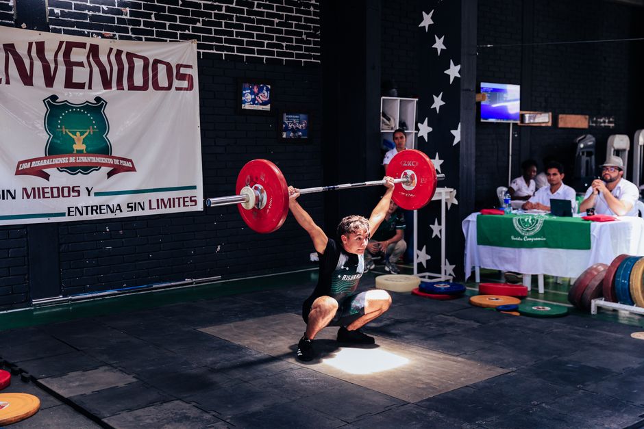 Atleta de levantamento de peso realizando um movimento de tira e arremesso em um evento de força e treinamento esportivo.