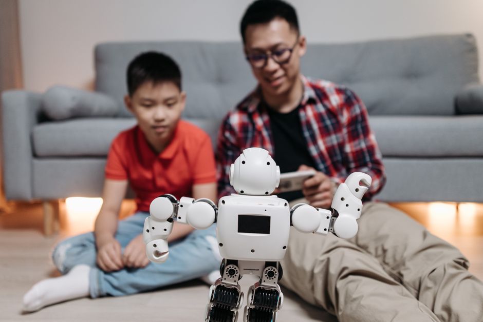 Pai e filho interagindo com um robô em um ambiente doméstico, simbolizando inovação tecnológica e educação infantil.